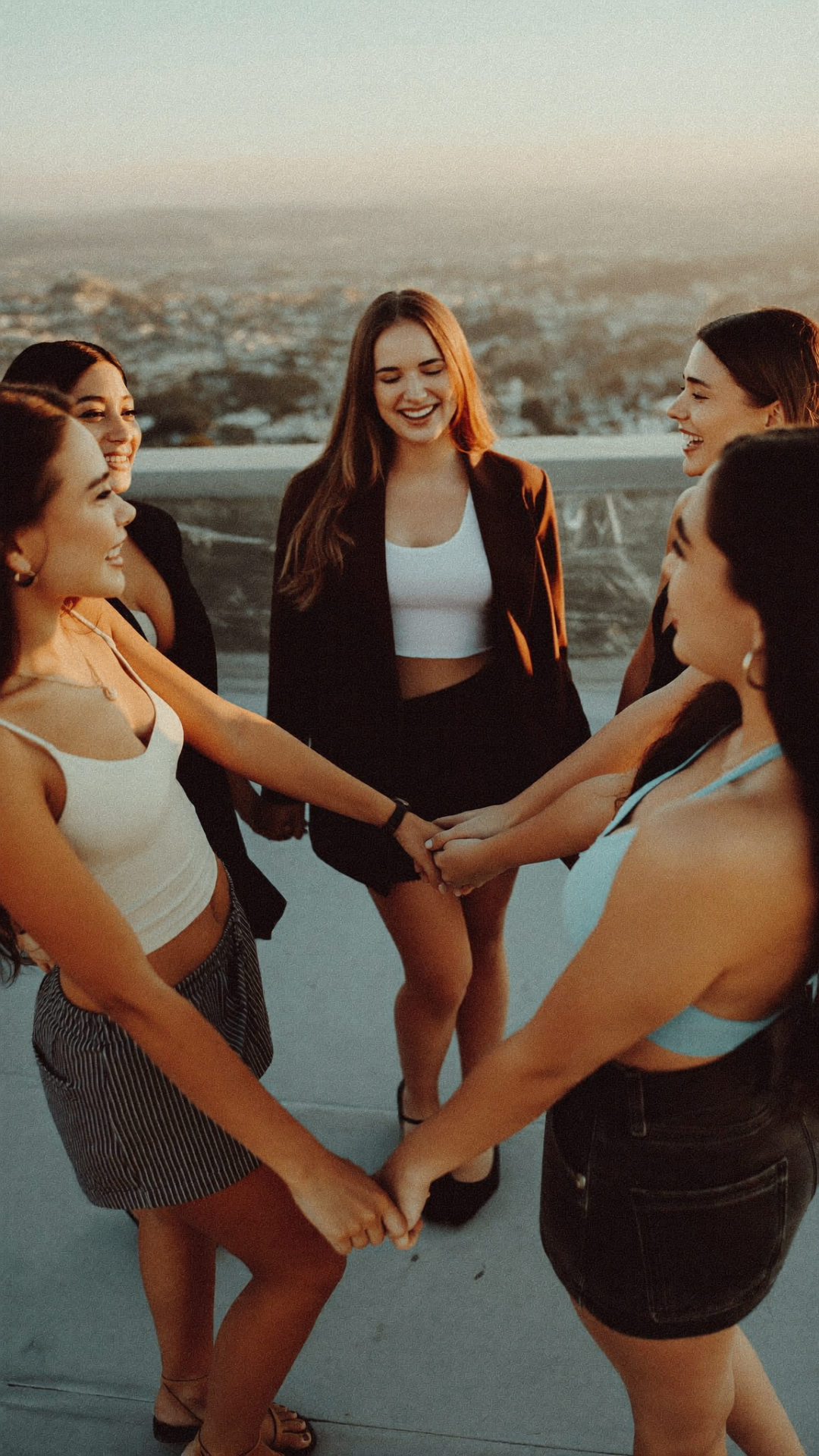 A circle of women holding hands at sunset